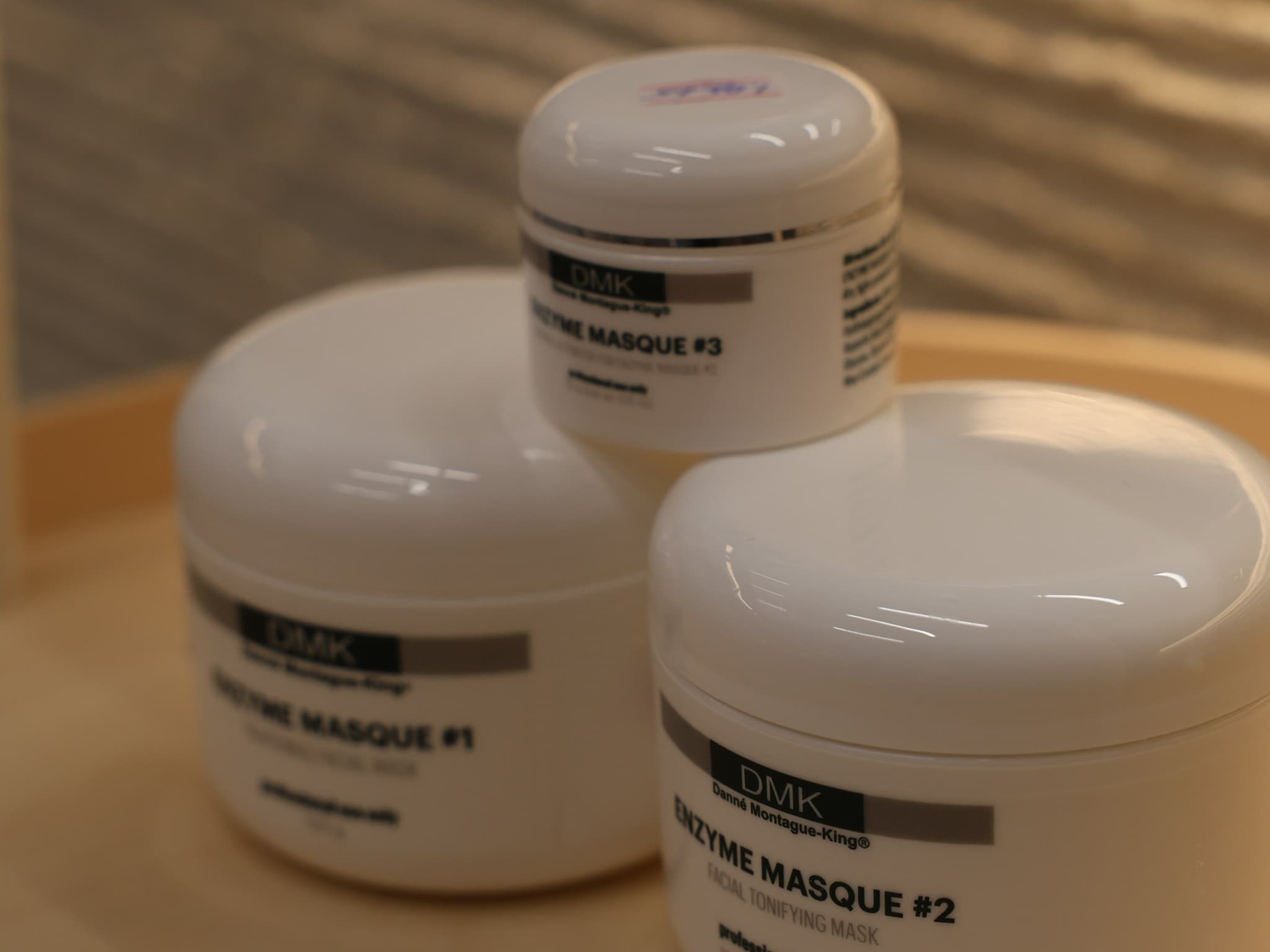 Three white DMK jars labelled Enzyme Masque #1, #2 and #3, stacked on a light wooden tray