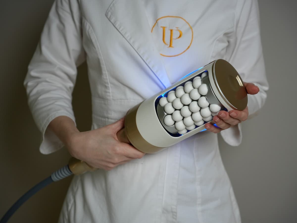 A therapist in a white UNIQUE PERSONA coat holding the Endosphere handpiece, its open drum of white silicone spheres lit blue