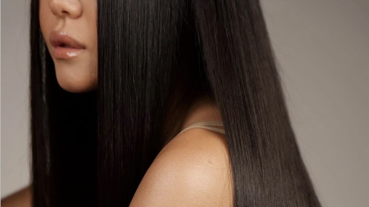 A woman photographed from the side, her long dark hair falling straight and glossy past her shoulder against a neutral backdrop