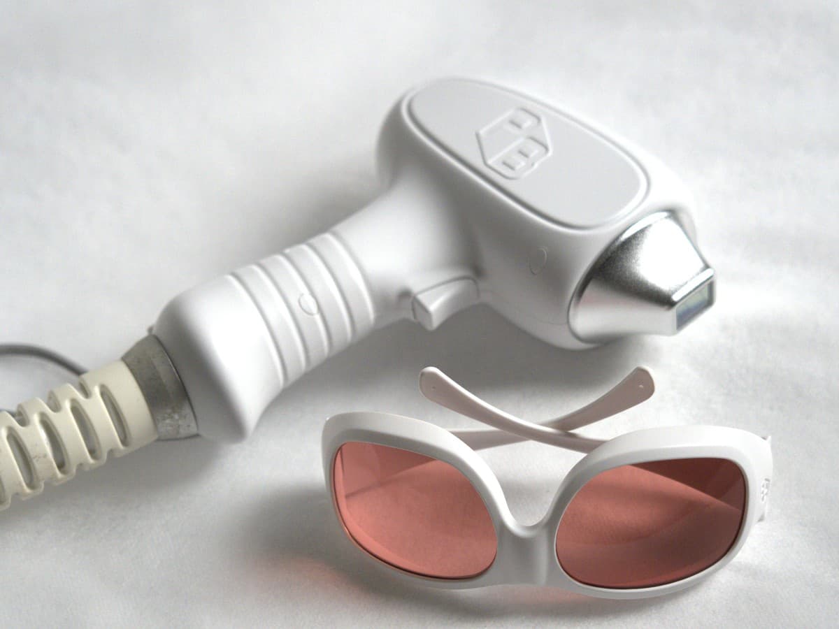 A white laser hair removal handpiece and rose-tinted protective goggles on a white surface