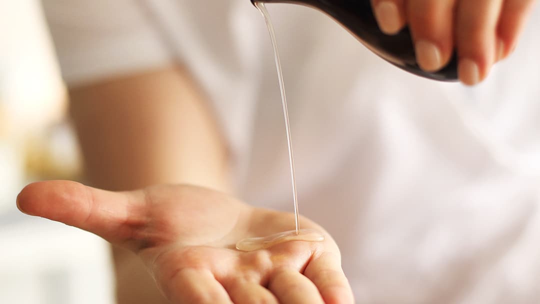 A therapist in white pouring massage oil into her palm