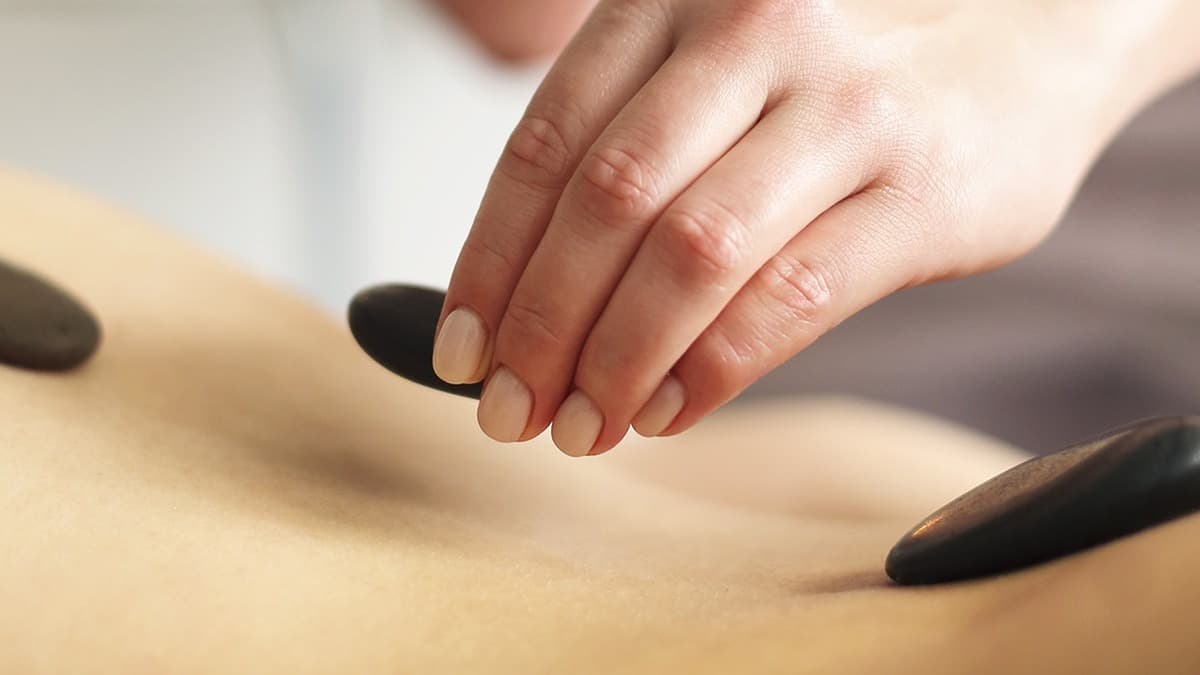 Hot stone massage, dark basalt stones being placed along a client's back