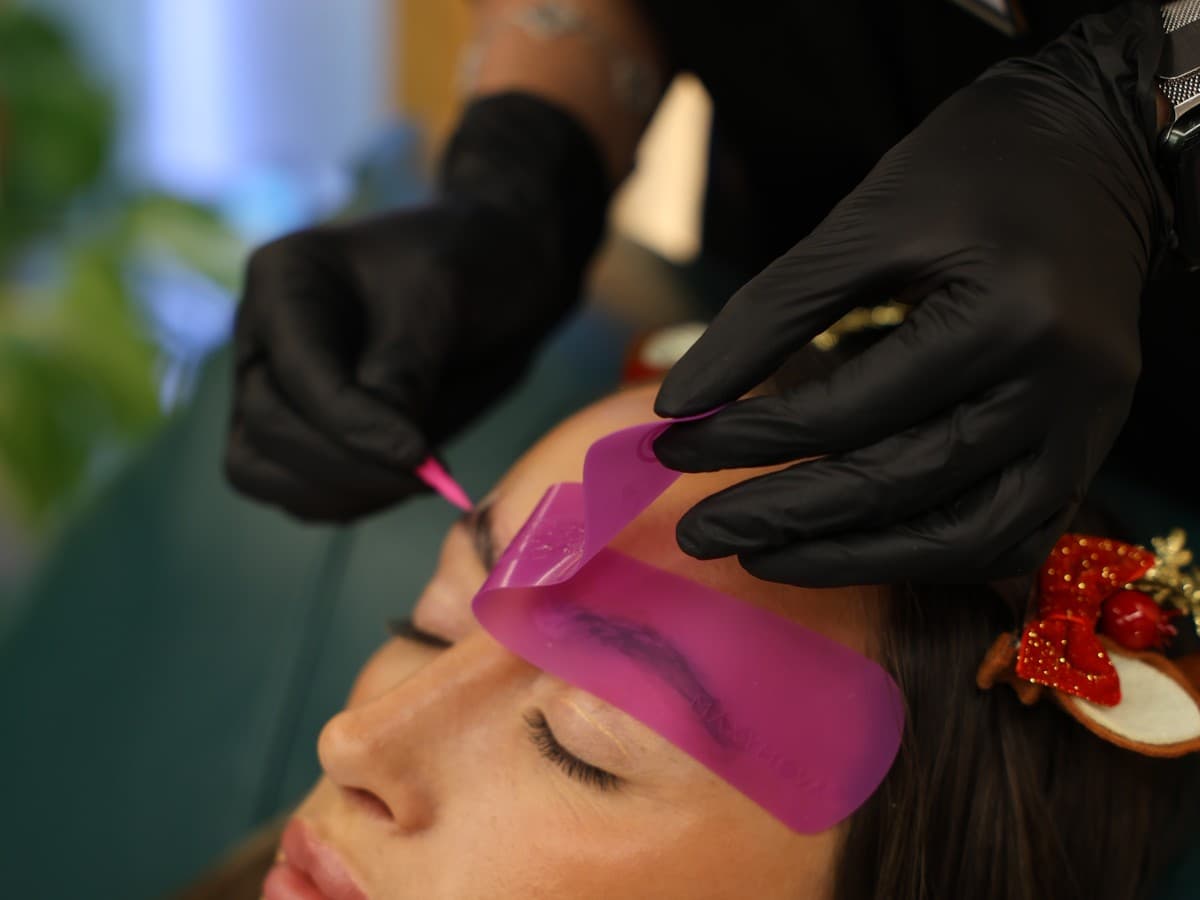A brow being treated behind a pink silicone shield, product applied with a fine brush, at UNIQUE PERSONA Dubai